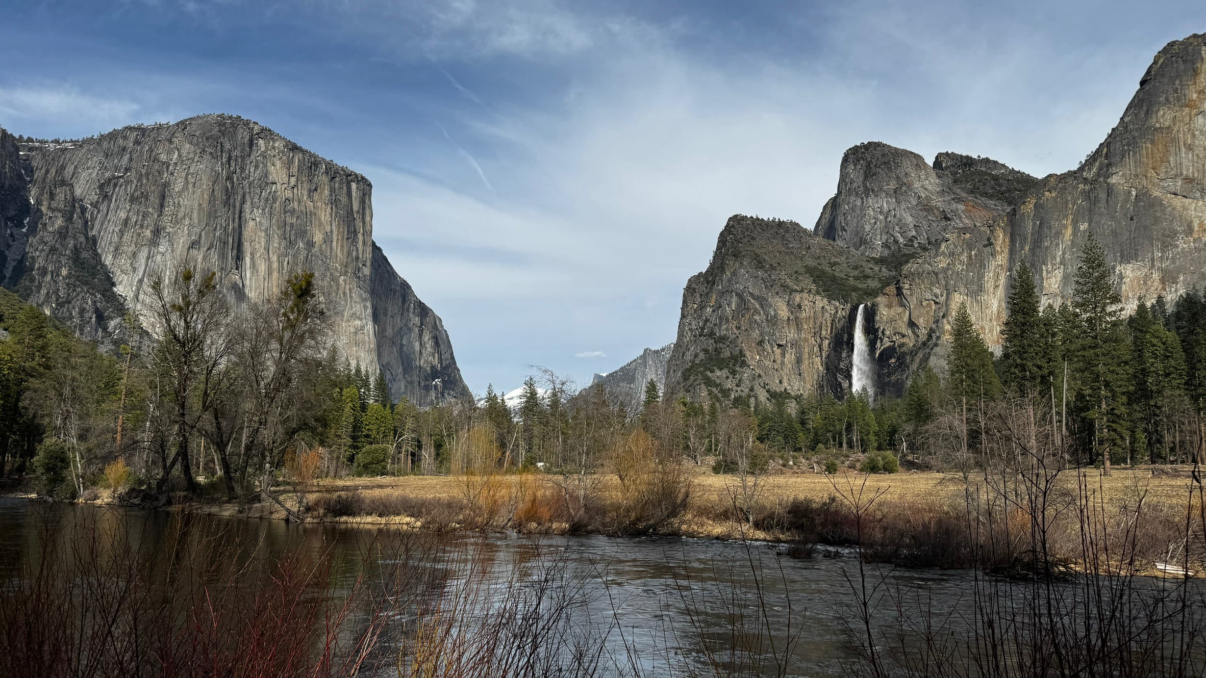 A river running through Yosemite Valley beneath granite cliffs and a waterfall